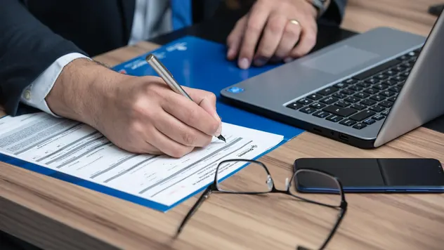 Business owner signing a legal document with a pen next to a laptop